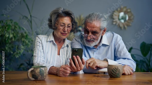 elderly people sitting at a table together watching social networks on the phone funny videos happy old age elderly couple pleasant memories leisure time in old age warm feelings support in old age