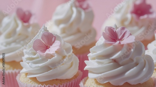 Sweet cupcakes decorated with cream and edible flowers on a pink background