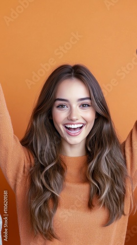 Beautiful young woman smiling joyfully against a vibrant orange backdrop in b...