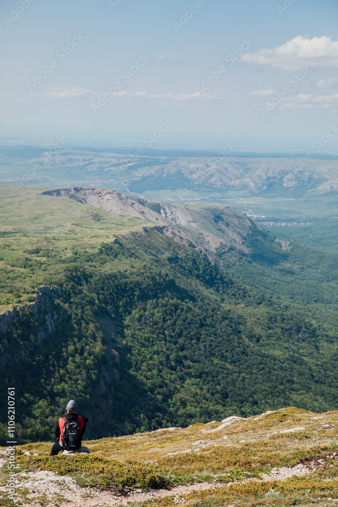 Male tourist resting and looking at the forest from the top of a mountain on a hike Male tourist resting and looking at the forest from the top of a mountain on a hike