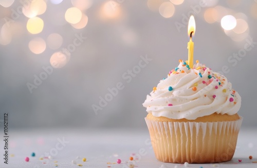 Colorful cupcake with candle and sprinkles on a background of soft lights
