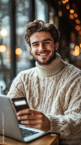 Smiling young man working on laptop in cozy cafe with credit card in hand