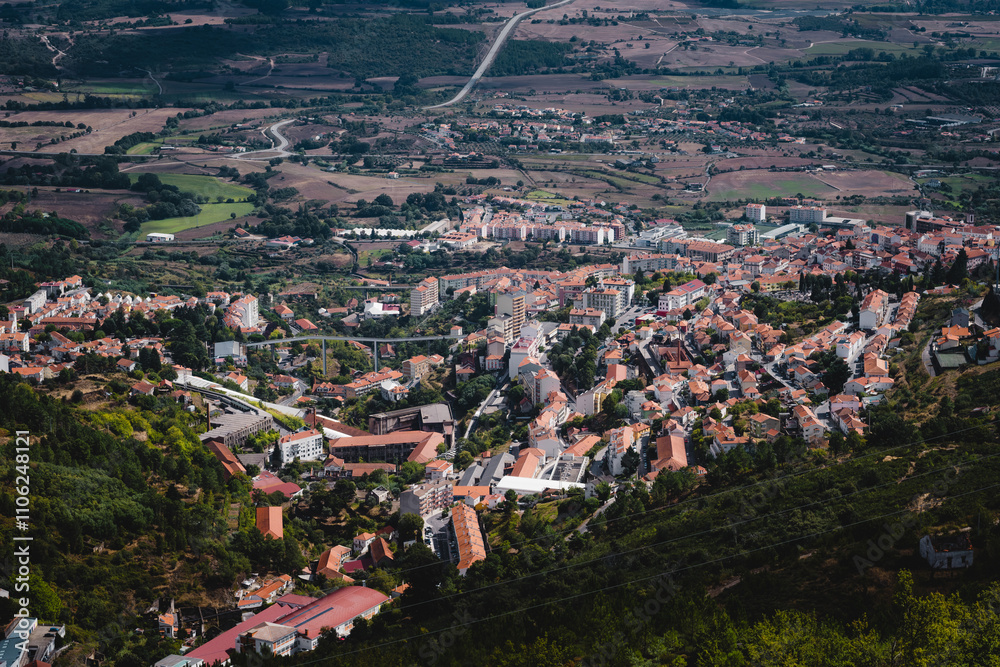 A view of a small town at the foot of Serra da Estrela in Portugal, nestled among rolling hills and surrounded by scenic mountain landscapes.