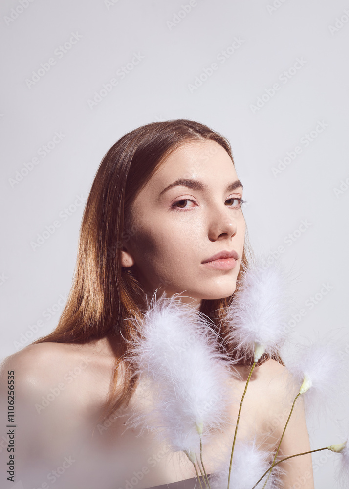 A beautiful brunette woman with fluffy plants in her hands poses on a light background. Demonstration of beautiful, healthy and well-groomed skin A beautiful brunette woman with fluffy plants in her hands poses on a light background. Demonstration of beautiful, healthy and well-groomed skin