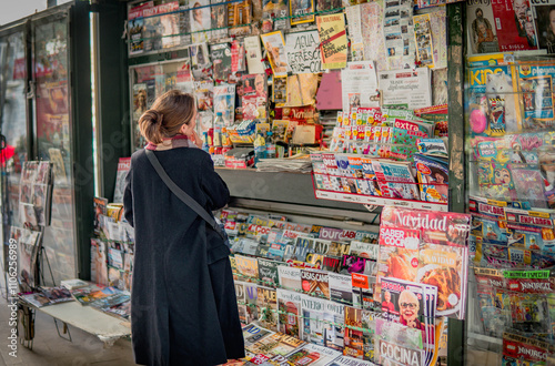 Hesitant Woman Looking at Magazines and Newspapers in a Street Kiosk, Thinking Which One to Buy. Traditional Press Concept photo