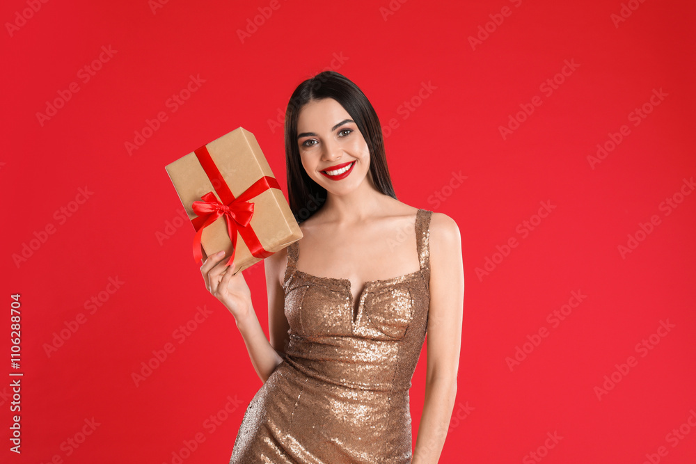 Woman in golden dress holding Christmas gift on red background Woman in golden dress holding Christmas gift on red background