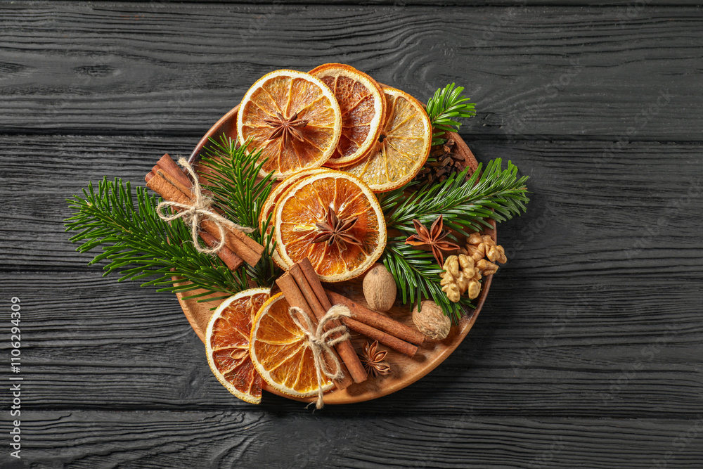 Different spices, dried orange slices and fir tree branches on black wooden table, top view. Christmas season