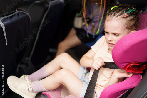 Cute little girl with dreadlocks fastening her seat belt in a car. Child safety concept in transport