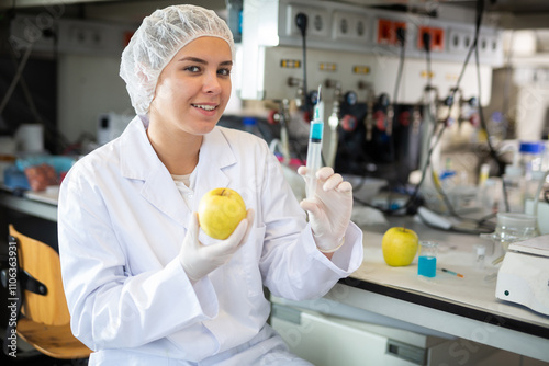 Professional female geneticist working in laboratory, injecting additives into apple during experiments with genetically modified apple