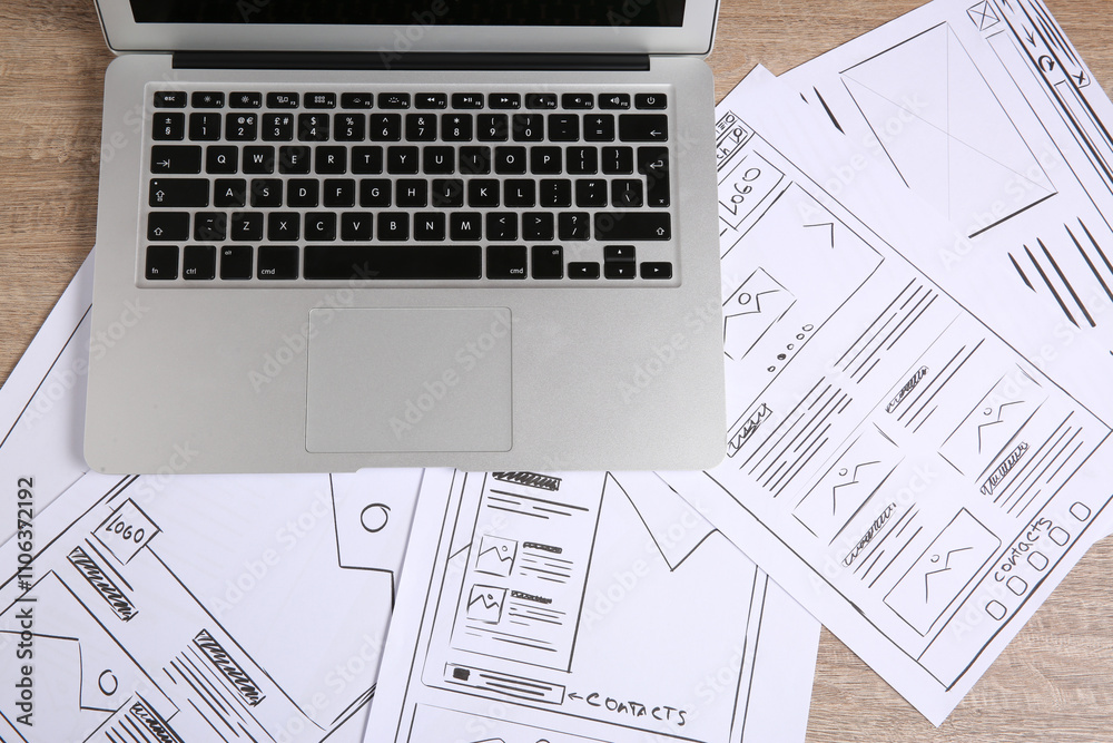 Developing UI design. Sketches of website wireframes and laptop on wooden table, top view Developing UI design. Sketches of website wireframes and laptop on wooden table, top view