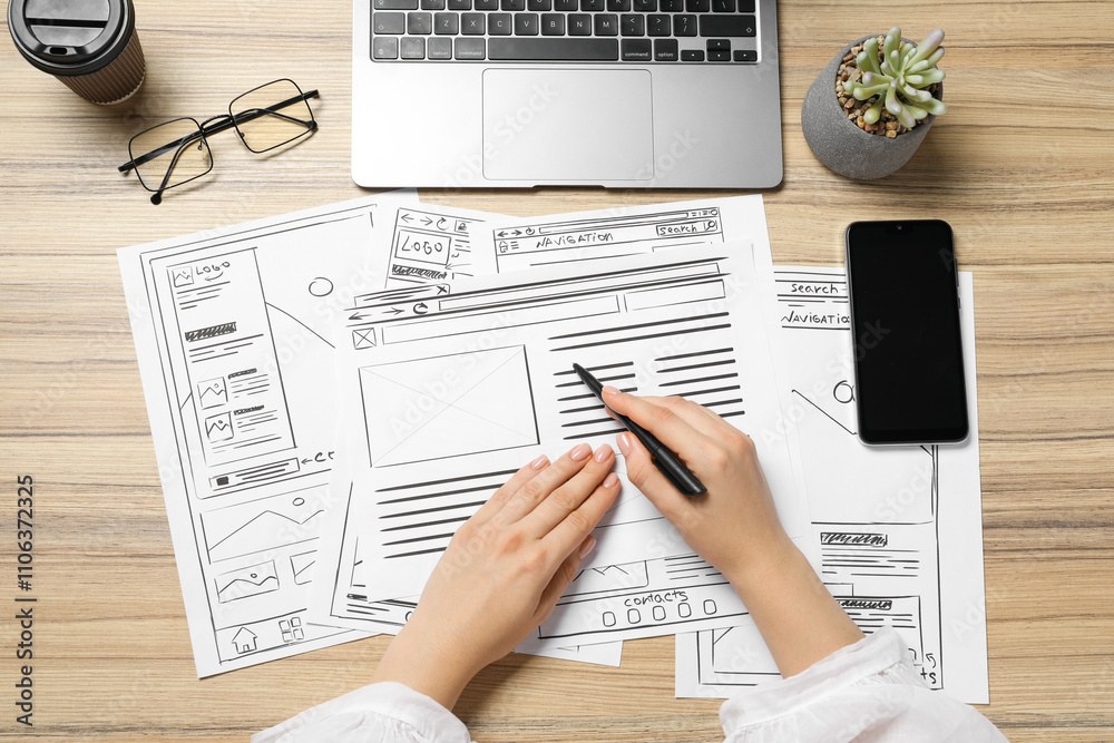 Website designer creating wireframe on paper with pen at wooden table, top view Website designer creating wireframe on paper with pen at wooden table, top view