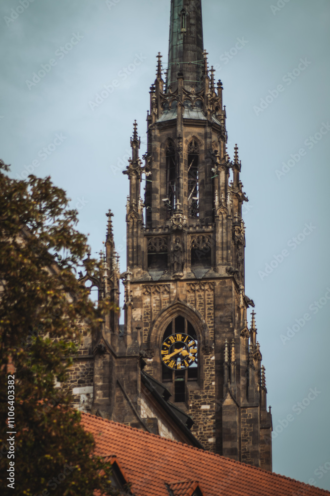 a tall, ornate Gothic-style church tower with a clock, surrounded by trees. The sky is overcast, creating a moody atmosphere a tall, ornate Gothic-style church tower with a clock, surrounded by trees. The sky is overcast, creating a moody atmosphere