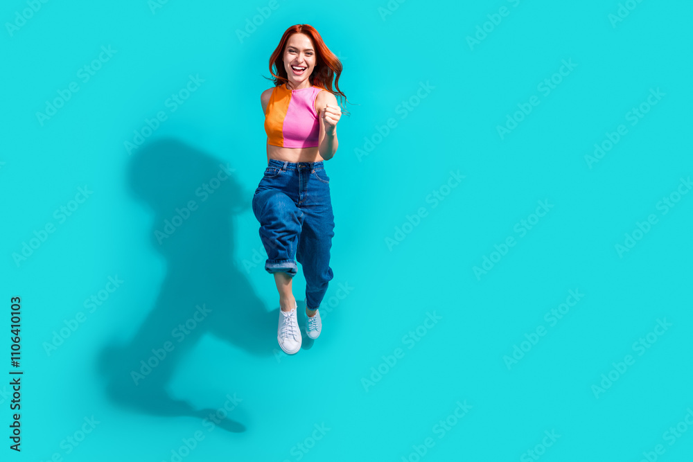 Joyful young woman with red hair jumping in summer outfit against vibrant teal background Joyful young woman with red hair jumping in summer outfit against vibrant teal background