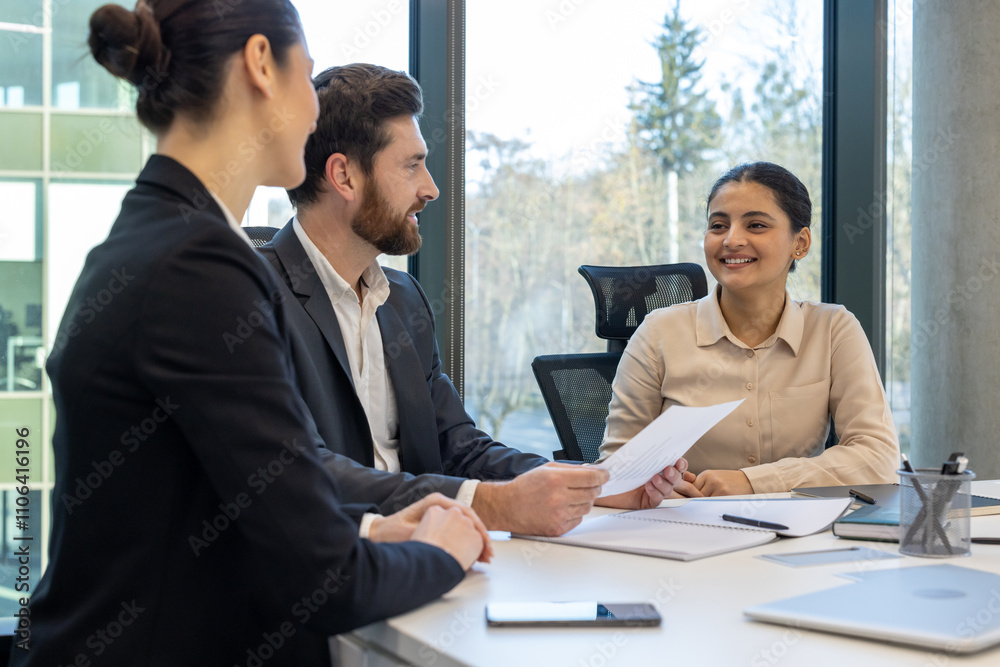 Job interview scene with young woman engaged with two professionals in bright office setting. People are seated at table with documents, discussing opportunities in modern workspace. Job interview scene with young woman engaged with two professionals in bright office setting. People are seated at table with documents, discussing opportunities in modern workspace.
