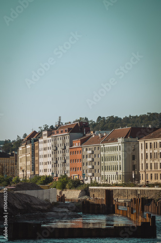 a tranquil riverside scene with colorful buildings lining the bank, lush greenery in the background, and clear blue skies reflecting off the water photo