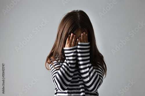 Scared little girl covering face with hands on grey background photo