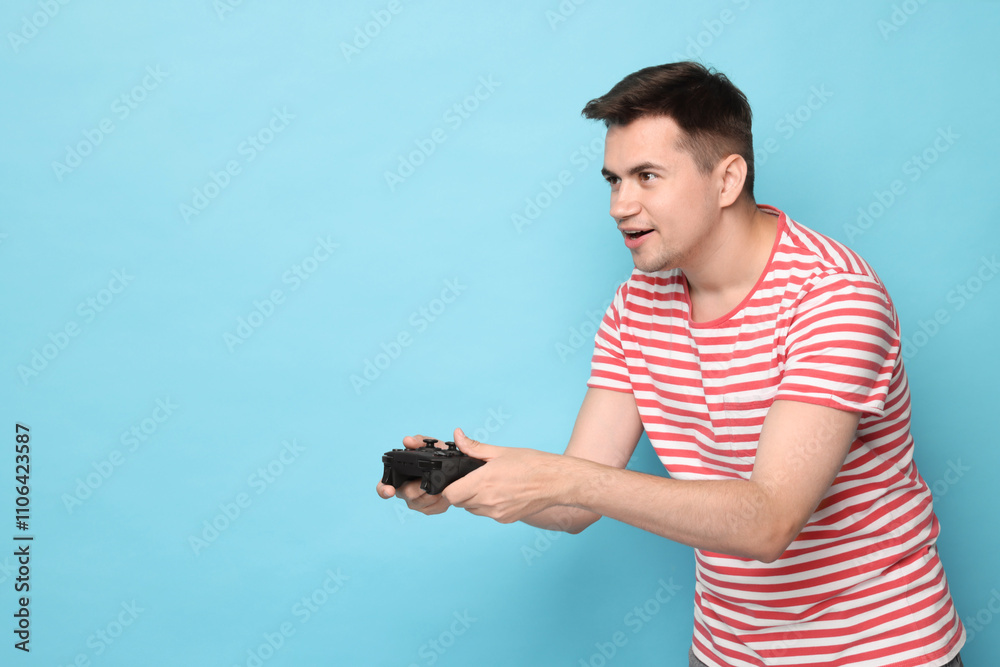Happy young man playing video games with controller on light blue background, space for text Happy young man playing video games with controller on light blue background, space for text