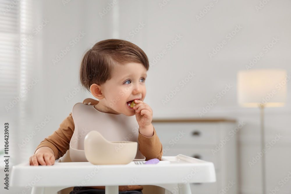 Cute little baby eating healthy food from bowl in high chair at home, space for text Cute little baby eating healthy food from bowl in high chair at home, space for text