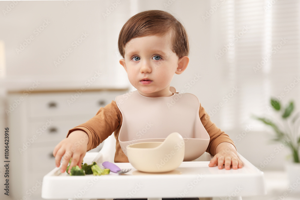Cute little baby eating healthy food from bowl in high chair at home Cute little baby eating healthy food from bowl in high chair at home