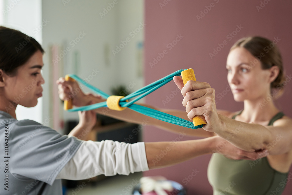 Physical therapist assisting woman by demonstrating exercise with resistance band Focused attention on correct technique while improving strength and flexibility Physical therapist assisting woman by demonstrating exercise with resistance band Focused attention on correct technique while improving strength and flexibility