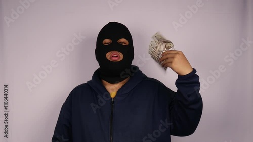 close up on the thief fanning his face using bundles of 100 dollar banknotes and wearing jacket with a white background
