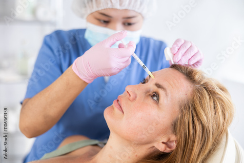 Qualified focused cosmetologist giving beauty injections for face skin rejuvenating and tightening for female client in aesthetic medicine office photo