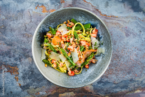 Traditional Italian Pasta with green Green asparagus, prawns and smoked salmon slices served with pine nuts and parmesan cheese slices as top view in a Nordic design bowl photo