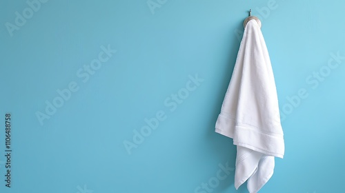 A white towel hanging on a hook against a light blue wall, creating a clean and minimalist aesthetic.