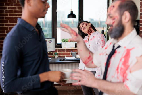 Fototapeta Man in blurry foreground starving for coffee in manager hands, while coworker in background mindlessly does tasks, being worked to death