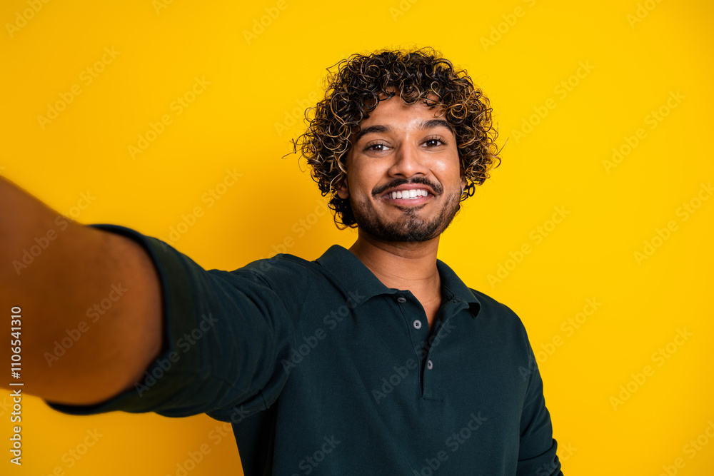 Cheerful young man in black shirt poses against vibrant yellow background capturing a joyful selfie Cheerful young man in black shirt poses against vibrant yellow background capturing a joyful selfie