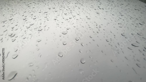 Raindrops on smooth surface create serene atmosphere, as water droplets reflect light, enhancing beauty of nature and calming weather of rainy day.