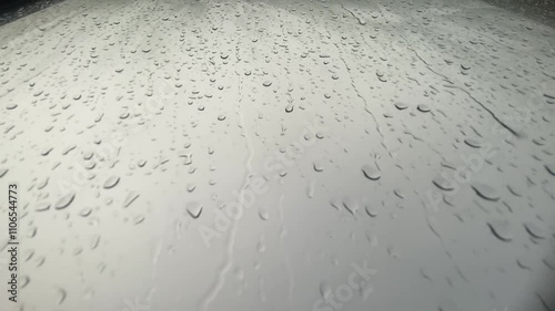 Raindrops on car window create tranquil atmosphere, as droplets of water reflect gray weather, capturing serene beauty of nature on rainy day.