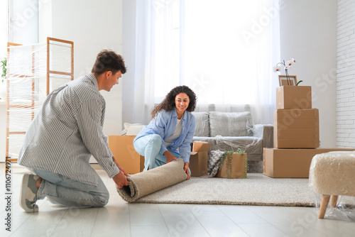 Young happy couple placing carpet near cardboard boxes in their new flat