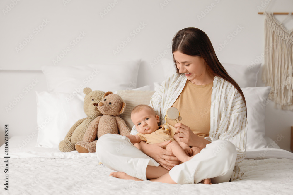 Happy mother with rattle and her little baby sitting in bedroom Happy mother with rattle and her little baby sitting in bedroom