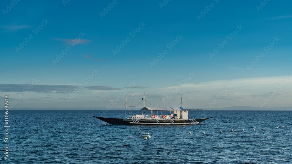 A beautiful traditional double-outrigger dugout bangka boat is anchored in the blue ocean. Life buoys on the railing. The awning over the deck. Ripples on the water. azure sky, clouds. Philippines. A beautiful traditional double-outrigger dugout bangka boat is anchored in the blue ocean. Life buoys on the railing. The awning over the deck. Ripples on the water. azure sky, clouds. Philippines.