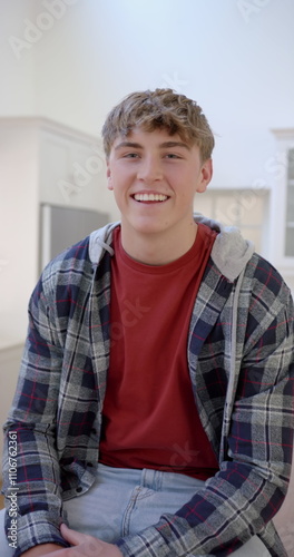 Vertical image of portrait of happy caucasian male teenager with blond hair at home, slow motion