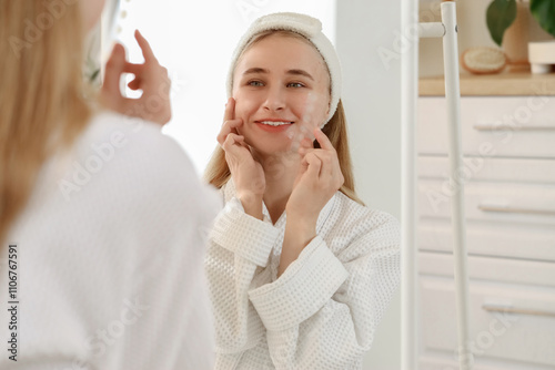 Young woman with acne problem and pimple patches near mirror in bathroom photo