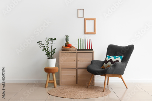 Interior of light room with armchair, candles and fruits for Kwanzaa celebration on drawers photo