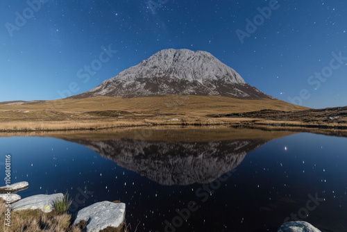 Mountain rising against starry night sky reflected in tranquil lake below. photo