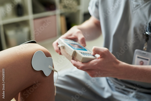 Conducting electrical stimulation therapy on patient's arm in clinical environment, using a handheld device and electrode connected to patient's skin. Image shows close-up view of treatment process