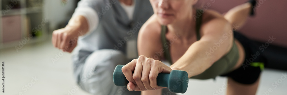 Close-up of person lifting dumbbells while engaging in workout routine in fitness studio, showcasing focus on strength training. Background features another individual joining the exercise activity Close-up of person lifting dumbbells while engaging in workout routine in fitness studio, showcasing focus on strength training. Background features another individual joining the exercise activity