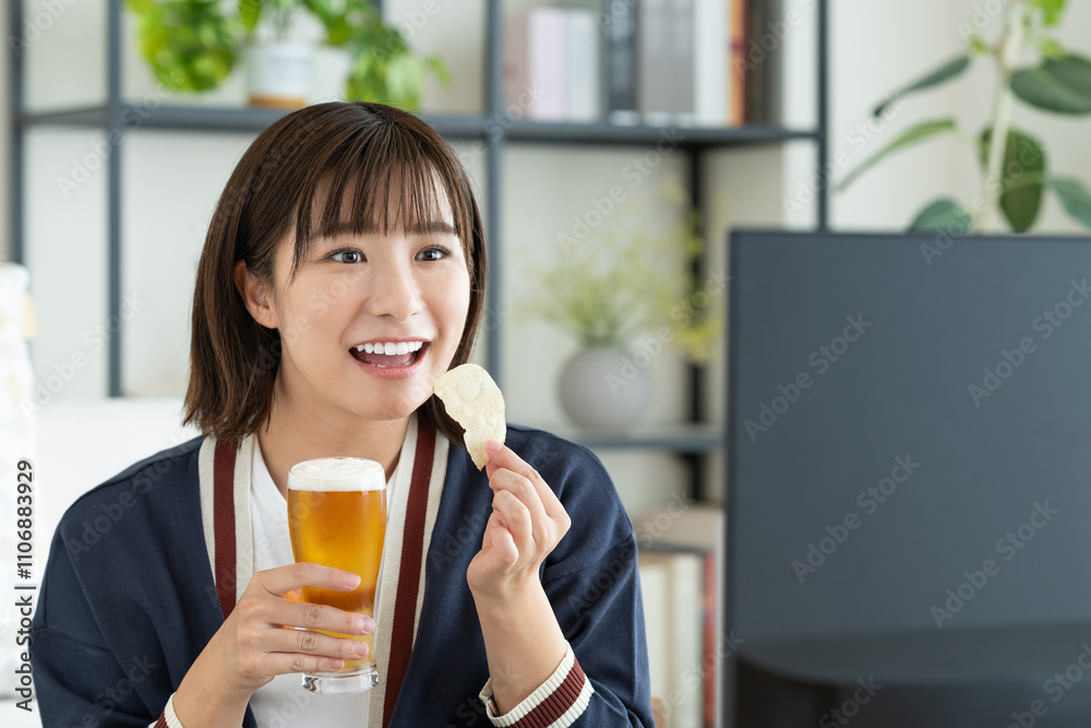 ビールを飲みながらテレビを見る若い女性 ビールを飲みながらテレビを見る若い女性
