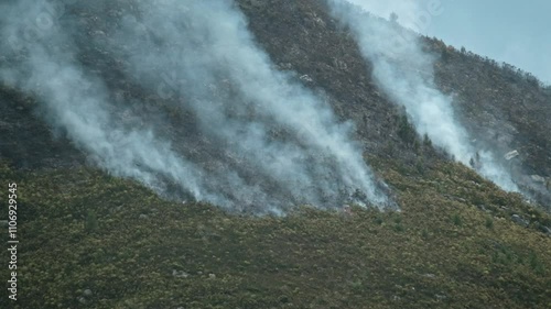 A wild fire smolders and burns on a mountainside in the South African Fynbos biome billowing smoke into the atmosphere photo