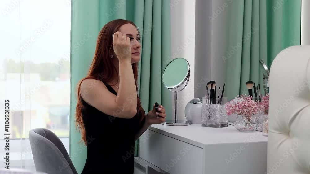 A girl in an evening dress applies powder to her face. Young attractive woman doing makeup behind a dressing table in slow motion