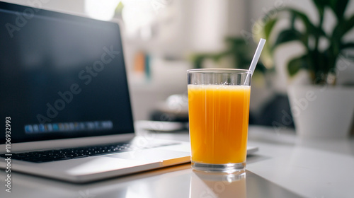 Refreshing orange juice next to a laptop on a modern workspace table in bright daylight