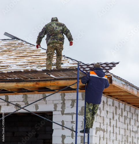 Two men are working on a roof, one of them is wearing a camouflage jacket photo