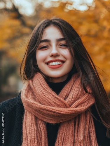 Cheerful young woman with winter scarf relaxing at park with yellow trees in background. Smiling beautiful girl enjoying warm sunny weather in autumn season. Happy pretty natural woman laughing.