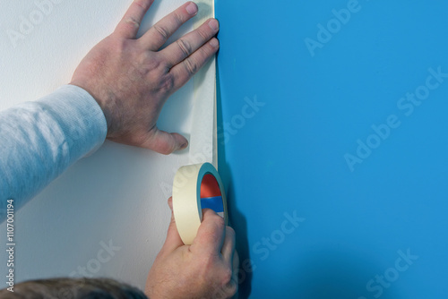 Application of masking tape to a wall is shown in close-up