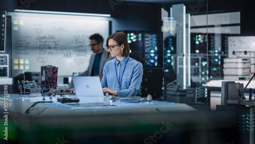 Portrait of Female Specialist Using Laptop Computer to Improve Electronic Circuit Board in Modern Office. Professional Engineer Thinking and Typing Ideas for Artificial Intelligence Project 