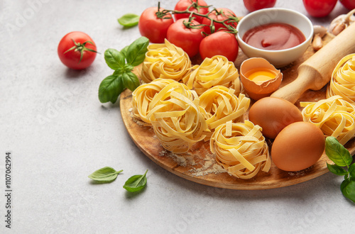 Fresh tagliatelle pasta nests with tomatoes, basil, eggs, flour and tomato sauce on wooden board